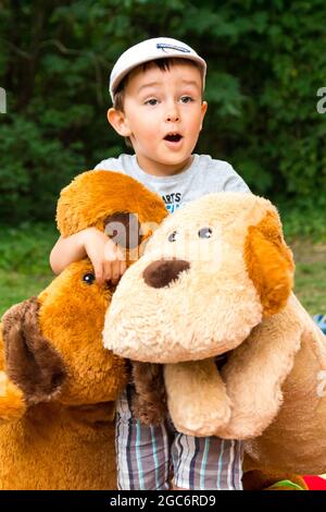 bambino di 4 anni con grandi cani peluche in piedi sorpresi con bocca aperta nel parco Foto Stock