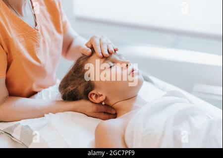 le mani reali del medico osteopath fa la terapia fisiologica ed impressionabile per la bambina di otto anni. sessione pediatrica di trattamento dell'osteopatia. alternativa Foto Stock