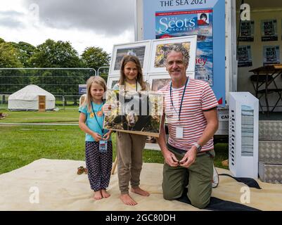 North Berwick, East Lothian, Scozia, Regno Unito, 7 agosto 2021. Gordon Buchanan a Fringe-by-the-Sea: Gordon Buchanan, noto fotografo di fauna selvatica e regista della serie TV 'Family & Me', insegni copie delle sue foto di fauna selvatica, qui con Aila Reid, di 5 anni, e Etta Reid, di 8 anni e una delle sue foto di orso Foto Stock