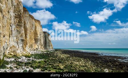 La scogliera di gesso si affaccia sulle rocce esposte sulla spiaggia con la bassa marea in una giornata estiva soleggiata con le nuvole di cumuli nel cielo blu. Foto Stock