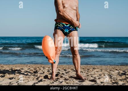 Sport nuotatore senior uomo formazione per nuotare in mare aperto triathlon con spiaggia sullo sfondo - anziani e stile di vita sano Foto Stock