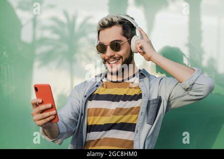 Un giovane hipster che ascolta la musica sull'app del telefono cellulare mentre indossa le cuffie all'aperto - concentrati sul viso Foto Stock