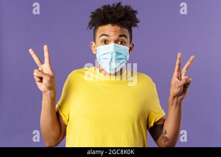 Medicina, covid19, coronavirus e concetto di persone. Upbeat, uomo ispanico con taglio di capelli afro, indossare maschera medica viso e mostrare segni di pace, rimanere Foto Stock