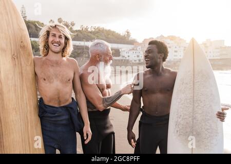 Diversi amici surfisti che tengono tavole da surf dopo una sessione di sport acquatici estremi con la spiaggia sullo sfondo - Focus su uomo anziano Foto Stock