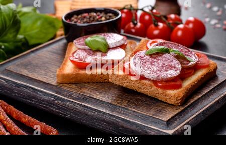 Salame spagnolo di salsiccia secca su fondo di cemento scuro. Preparazione di deliziosi panini freschi Foto Stock