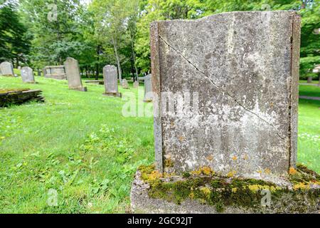 Un vecchio, muschio coperto, e rotto marcatore tomba in un cimitero. Nessun contrassegno visibile. Altre lapidi dietro. Rotto in alto. Foto Stock