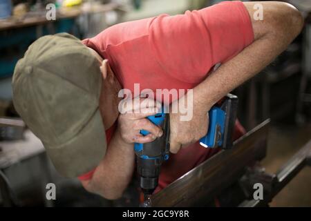 Un uomo perfora i fori nel metallo. Il ragazzo lavora in officina. Punta per lavori pesanti. Mio padre lavora nel garage. Foto Stock