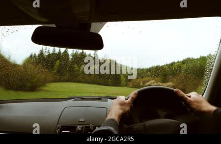 Guida di un moderno fuoristrada guida a destra RHD auto sulla montagna verde foresta di campagna strada in un giorno di pioggia moody. Vista sul parabrezza dell'auto POV Foto Stock