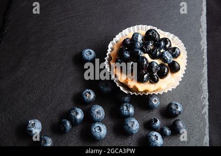 Crostata con mirtilli è su uno sfondo nero di pietra naturale. Ancora vita con dolci dolci con frutti di bosco su sfondo scuro Foto Stock