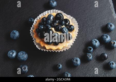 Crostata con mirtilli è su uno sfondo nero di pietra naturale. Ancora vita con dolci dolci con frutti di bosco su sfondo scuro Foto Stock