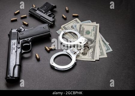 Denaro e punizioni penali. Pistole e proiettili da 9 mm, manette e banconote in dollari americani su sfondo nero. Concetto di criminalità e diritto, Foto Stock