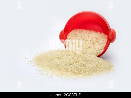 Il riso secco non fatto cadere da una piccola ciotola rossa su uno sfondo bianco isolato Foto Stock