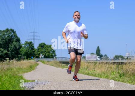 Vista ad angolo basso di un uomo anziano che lavora a fare jogging contro un cielo blu chiaro e soleggiato con copyspace in un concetto di salute e fitness e stile di vita attivo Foto Stock