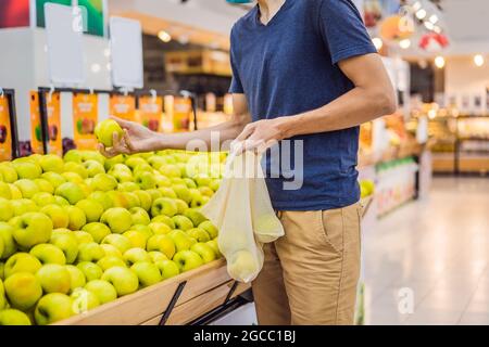 L'uomo sceglie le mele in un supermercato senza usare un sacchetto di plastica. Sacchetto riutilizzabile per l'acquisto di verdure. Concetto di zero sprechi Foto Stock