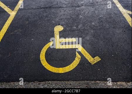 Il parcheggio per disabili è contrassegnato da un cartello giallo dipinto sulla strada Foto Stock
