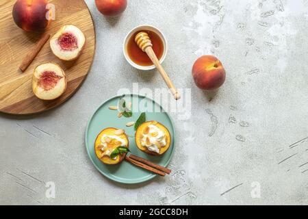 Pesche mature al forno con cannella, petali di mandorle, formaggio cremoso e miele su un fondo di cemento chiaro. Foto Stock