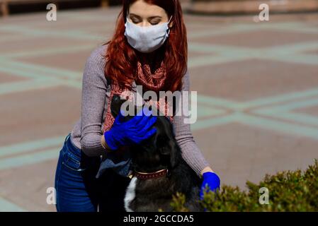Giovane donna che usa una maschera facciale come un coronavirus che diffonde prevenzione camminare con il suo cane. Immagine globale del concetto pandemico COVID-19. Foto Stock