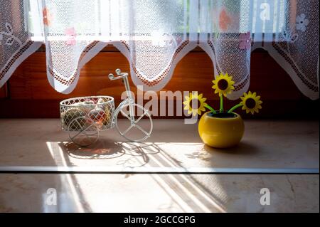 Vista su un girasole artificiale in plastica alimentato a energia solare che si muove dalla luce solare che rappresenta una fonte di energia rinnovabile nella finestra. Foto Stock