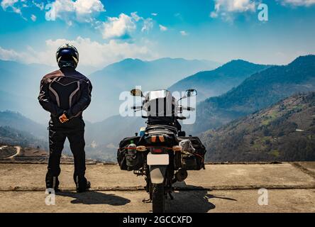 l'uomo motociclista che guarda la valle dalla cima della collina con la sua moto caricata e immacolata immagine della vista naturale è preso a bomdilla arunachal pradesh india. Foto Stock