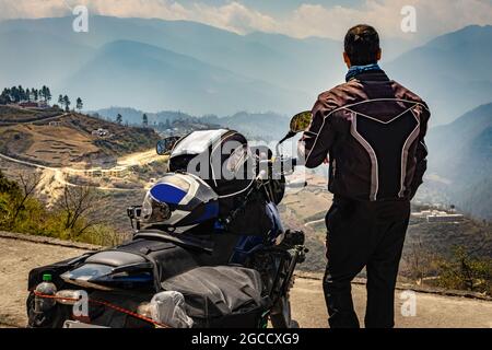 l'uomo motociclista che guarda la valle dalla cima della collina con la sua moto caricata e immacolata immagine della vista naturale è preso a bomdilla arunachal pradesh india. Foto Stock