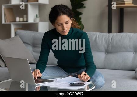 Donna focalizzata che usa il computer portatile e la calcolatrice, controllando le fatture domestiche Foto Stock