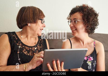 La donna anziana è felice di imparare a utilizzare i social network, mentre la giovane figlia spiega come utilizzare il tablet Foto Stock