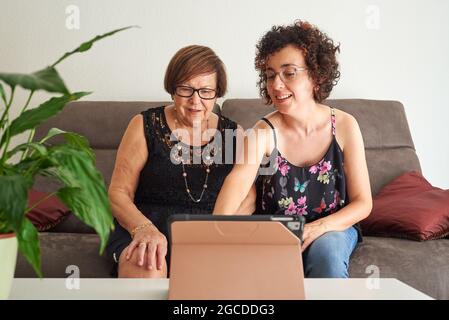 La giovane donna insegna alla madre anziana come usare il tablet digitale Foto Stock