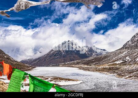 montagna con copertura della neve con cielo drammatico attraverso il blurred buddismo bandiere cornice al giorno l'immagine è presa al passo di sela tawang arunachal pradesh india. Foto Stock