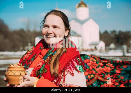 Ritratto di sconosciuta bella ragazza giovane donna con scarafetta sulle spalle e pentola in mano alla celebrazione di Maslenitsa Shrovetide vacanza in Foto Stock
