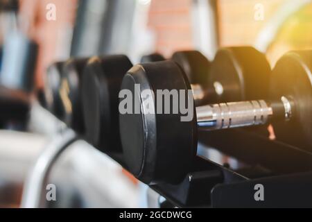 Primo piano molti manubri in metallo su rack nella sala fitness con muro in mattoni Bacckground. Attrezzature per l'addestramento del peso. Foto Stock