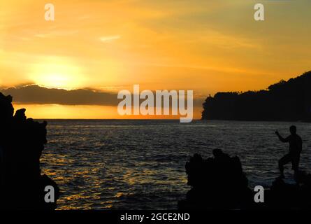 Nativo Hawaiiano sale le bracie marine di Laupahoehoe Beach Park. Indica il tramonto come incoraggiare gli altri ad apprezzare la sua bellezza. Foto Stock