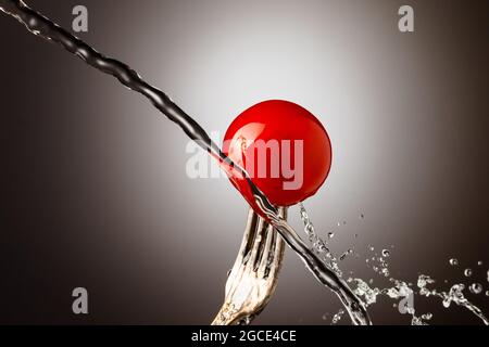pomodoro di ciliegio su una forchetta d'argento, getto d'acqua, spray Foto Stock