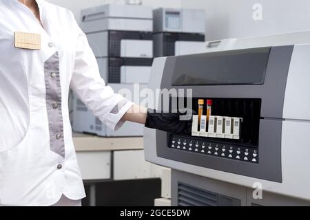 Ricercatore femminile che inserisce la provetta con il campione di sangue nella macchina medica dell'analizzatore. Lo scienziato lavora con l'apparecchiatura medica moderna in Foto Stock
