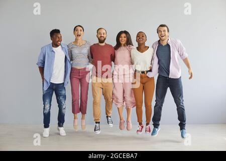Gruppo vario di giovani uomini e donne felici ed eccitati in abiti casual che saltano in studio Foto Stock
