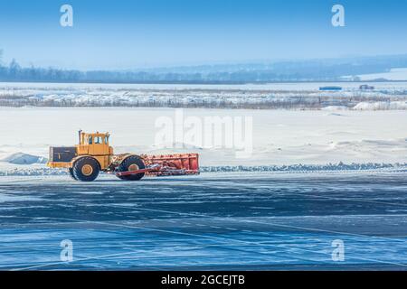 Un trattore con benna pulisce l'asfalto dalle derive di neve. Concetto di servizi comunali e di lavoro Foto Stock