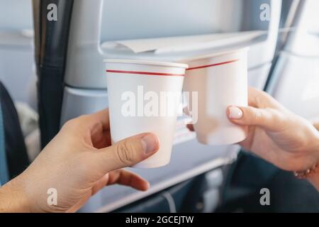 L'uomo felice e una donna si aggraffano i bicchieri di carta all'interno di un aereo durante un volo di vacanza. Catering e degustazione di vini Foto Stock