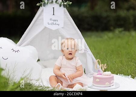 Bella sessione fotografica allestita per la bambina che festeggia un anno di compleanno, all'aperto in estate con wigwam bianco, coperta, palloncino. Delizioso Foto Stock