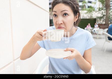 Donna prende un sorso di caffè e fa un disgustoso rimace. Il concetto di cattivo odore o difficoltà a svegliarsi e insonnia Foto Stock