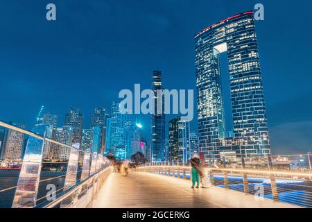 Vista panoramica del ponte pedonale con turisti che conducono a numerosi grattacieli con alberghi ed edifici residenziali sulla costa del Golfo Persico a Dubai du Foto Stock