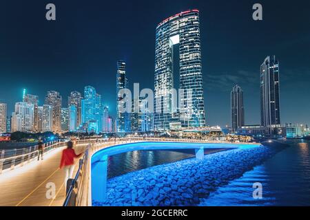 Lunga esposizione vista panoramica del ponte pedonale con turisti che conduce a numerosi grattacieli con alberghi ed edifici residenziali sul Golfo Persico coa Foto Stock