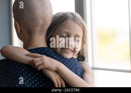 Felice figlia capretto che abbraccia la mamma del cancro con gli occhi chiusi Foto Stock