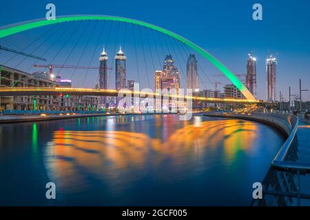 Illuminato in verde Tolerance Bridge a Dubai con un insolito design architettonico sullo sfondo di grattacieli. Urbanismo e avvistamento Foto Stock