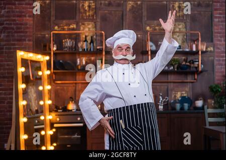 Uno chef professionista, anziano e cordiale, che indossa un grembiule e un cappello Foto Stock