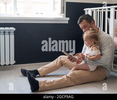 Un padre premuroso legge una fiaba alla sua figlia piccola nella camera dei bambini. Foto Stock