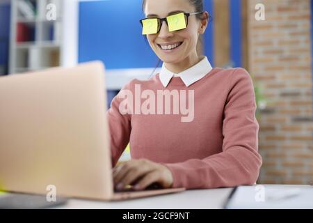 Giovane donna sorridente con stickar gialli sugli occhiali con punto interrogativo funziona sul laptop Foto Stock