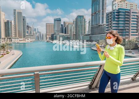 La donna asiatica è impegnata nella passeggiata sportiva nella zona di Dubai Marina e indossa una maschera medica protettiva a causa della pandemia del coronavirus e utilizza un intelligente Foto Stock