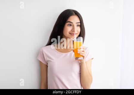 Felice donna indiana che tiene un bicchiere di succo di frutta, avendo una bevanda rinfrescante a casa. Ritratto di allegra signora asiatica gustando una bevanda gustosa. Detox, weig Foto Stock