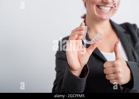 Una donna in una giacca mostra i pollici verso l'alto e mostra le guardie della bocca per allineare il morso. La ragazza approva i rinforzi rimovibili in plastica per il Foto Stock