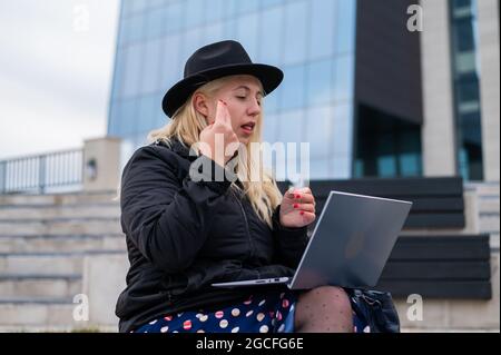 La giovane donna parla il linguaggio dei segni durante una videochiamata su un computer portatile all'aperto. La ragazza sordomuta comunica con i gesti Foto Stock