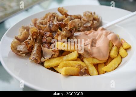 Donare carne kebab da uno spiedo turco rotante con patatine fritte e salsa cocktail su un piatto bianco in un ristorante fast food, focalizzato selezionato, stretto Foto Stock